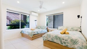 A modern bedroom with two single beds, a ceiling fan, and large windows with blinds.