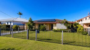 A residential property with a fenced yard, solar panels on the roof, and a clear blue sky.