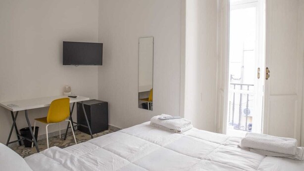 Une chambre d’hôtel comprenant un lit, un bureau avec une chaise, une télévision et une porte donnant sur un balcon.