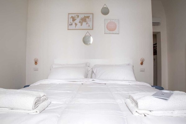 Un lit bien fait, avec du linge de lit et des serviettes blanches, une carte du monde et une affiche sur le mur avec l’inscription « Esprit serein ».