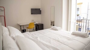 Une chambre d’hôtel équipée d’un lit, d’un bureau, d’une chaise, d’une télévision et d’une fenêtre donnant sur un balcon.