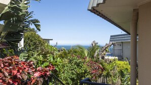 A balcony with a view of the ocean, surrounded by tropical plants.
