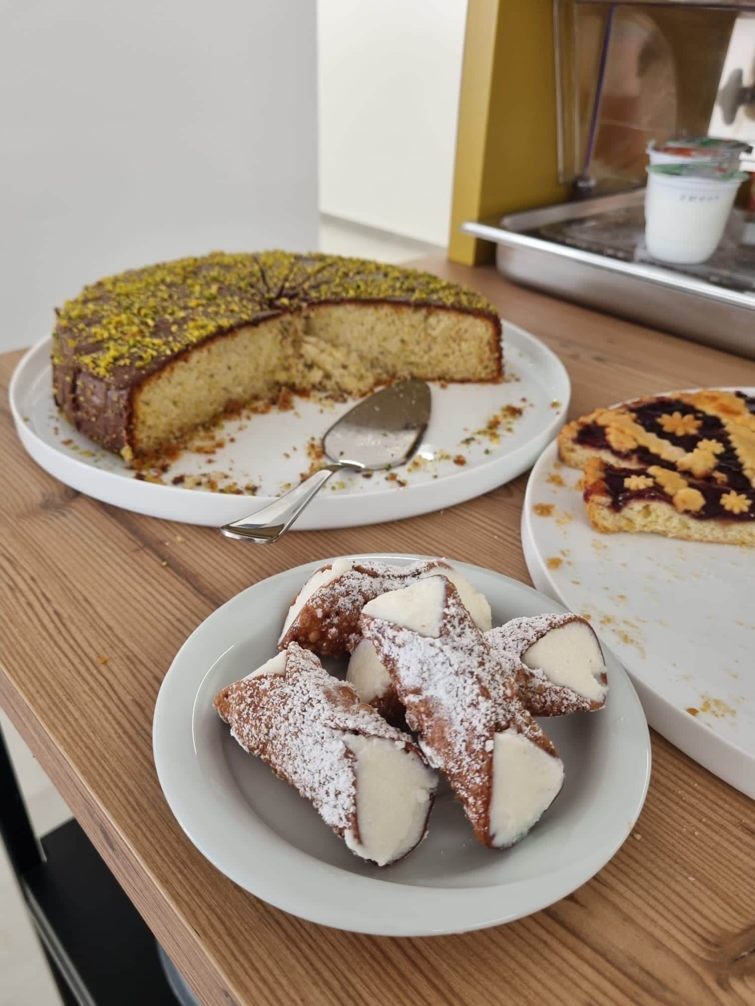 Une table en bois avec un gâteau, une assiette contenant des morceaux de dessert et une tarte à laquelle on a déjà coupé une part.