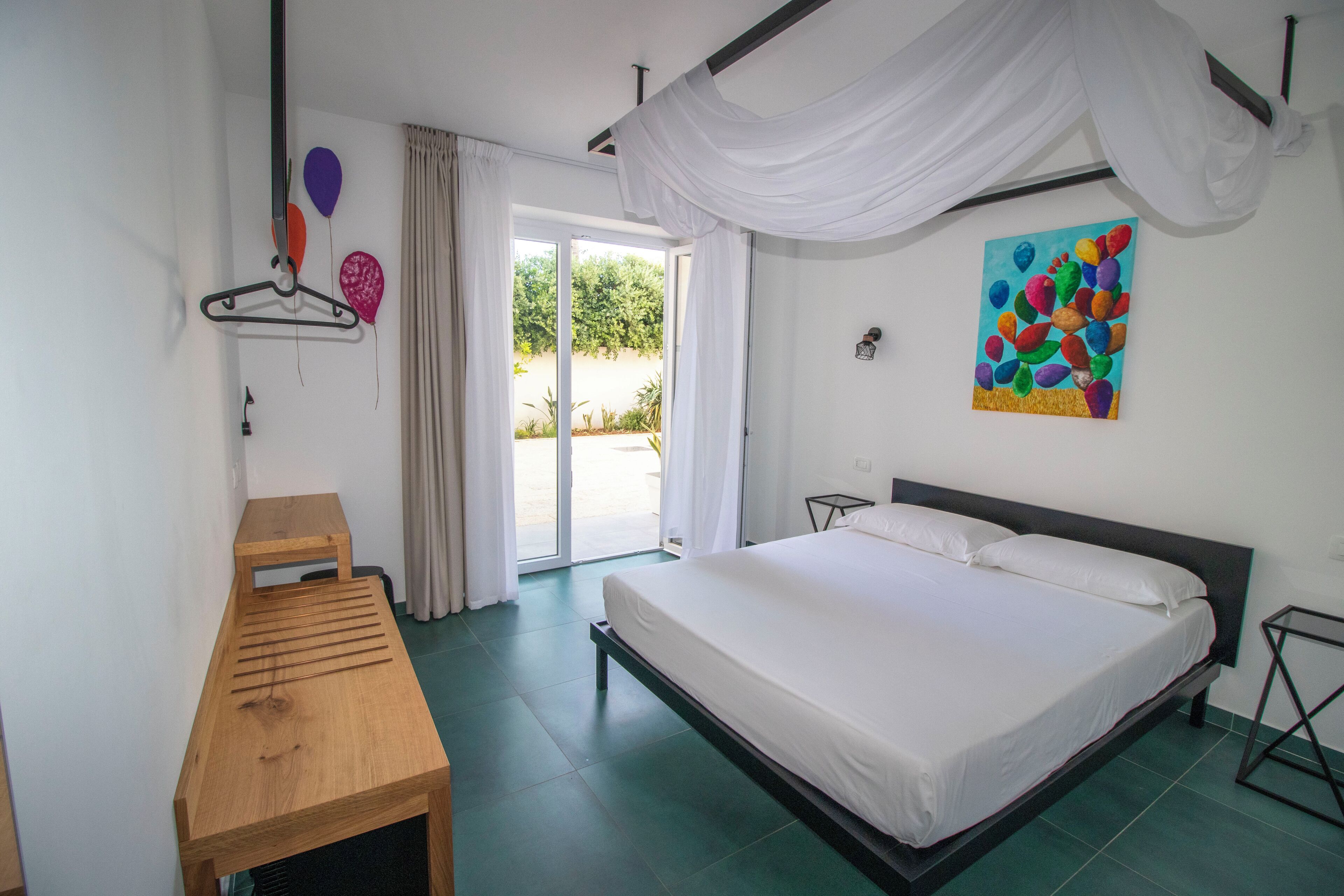 A bedroom with a bed, a wooden table, a painting, and a view through the door.