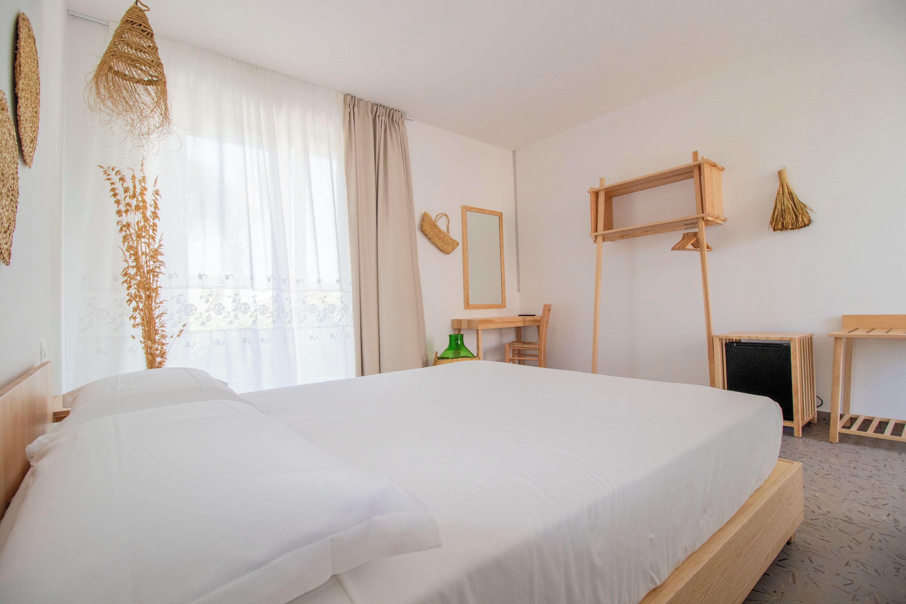 Habitación de hotel ordenada con una cama grande, un escritorio, una silla, un espejo y una mesita.
