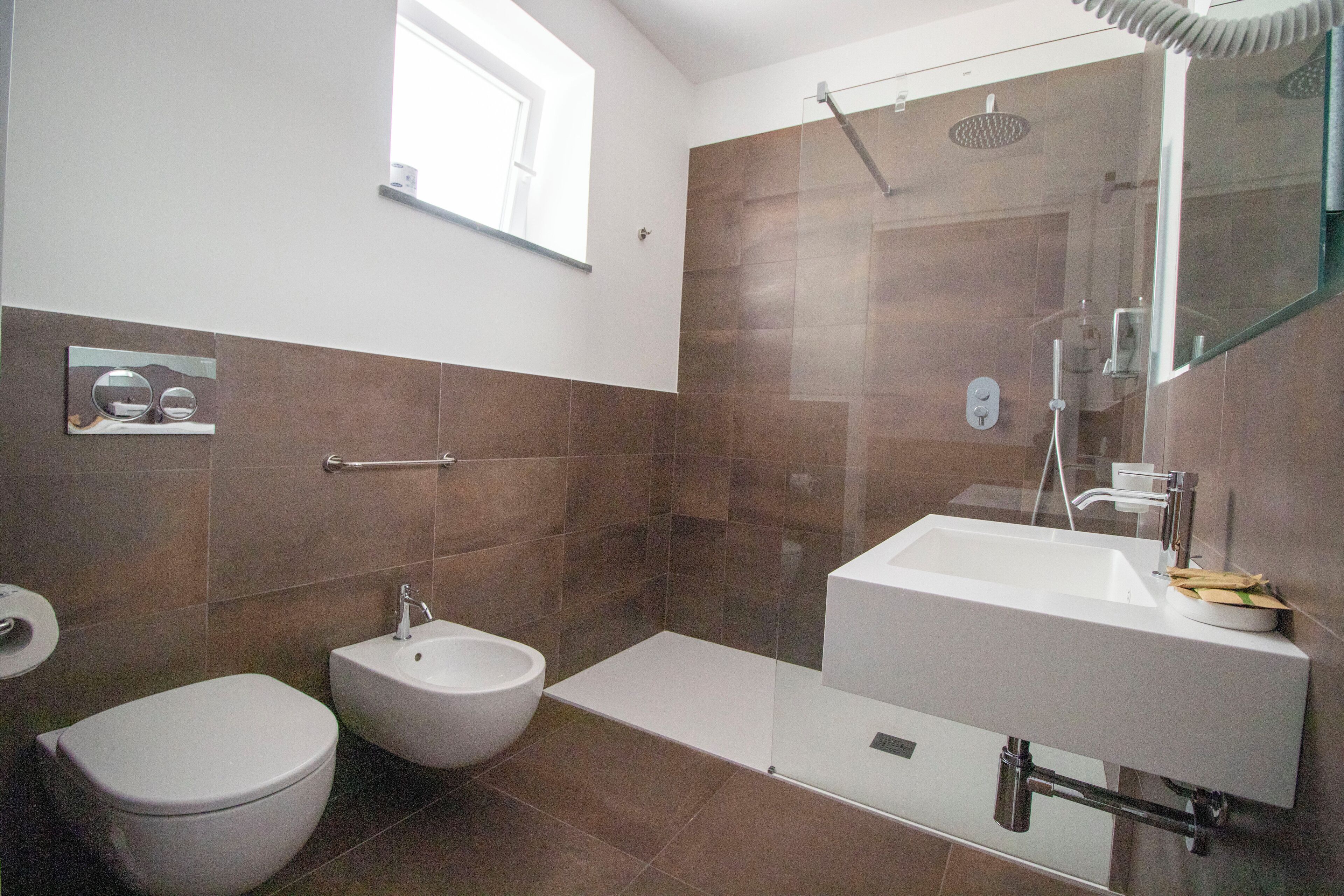 A modern bathroom with a toilet, bidet, and a large sink with a mirror.