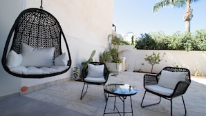 A hanging chair, two chairs, and a table in an outdoor patio area with plants and a palm tree. - Hotel Arte Mare (San Vito Lo Capo)