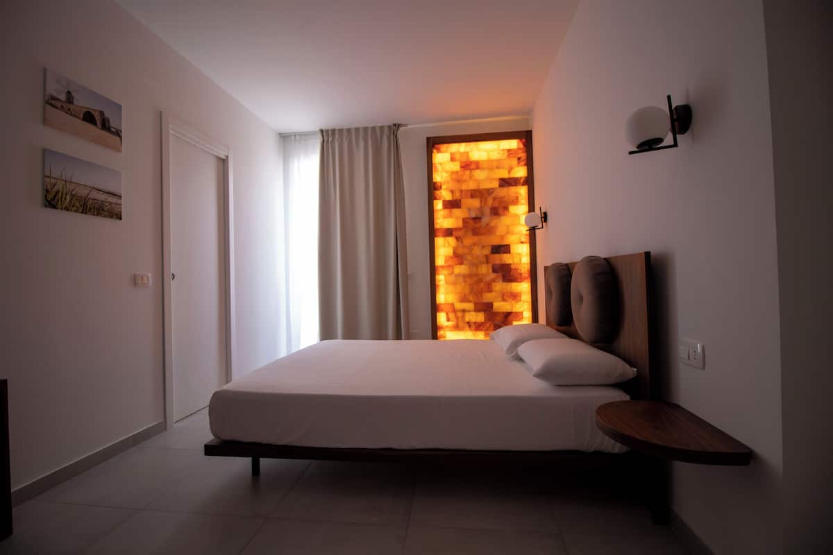 A modern bedroom with a bed, a nightstand, a wall-mounted lamp, and a wooden headboard.