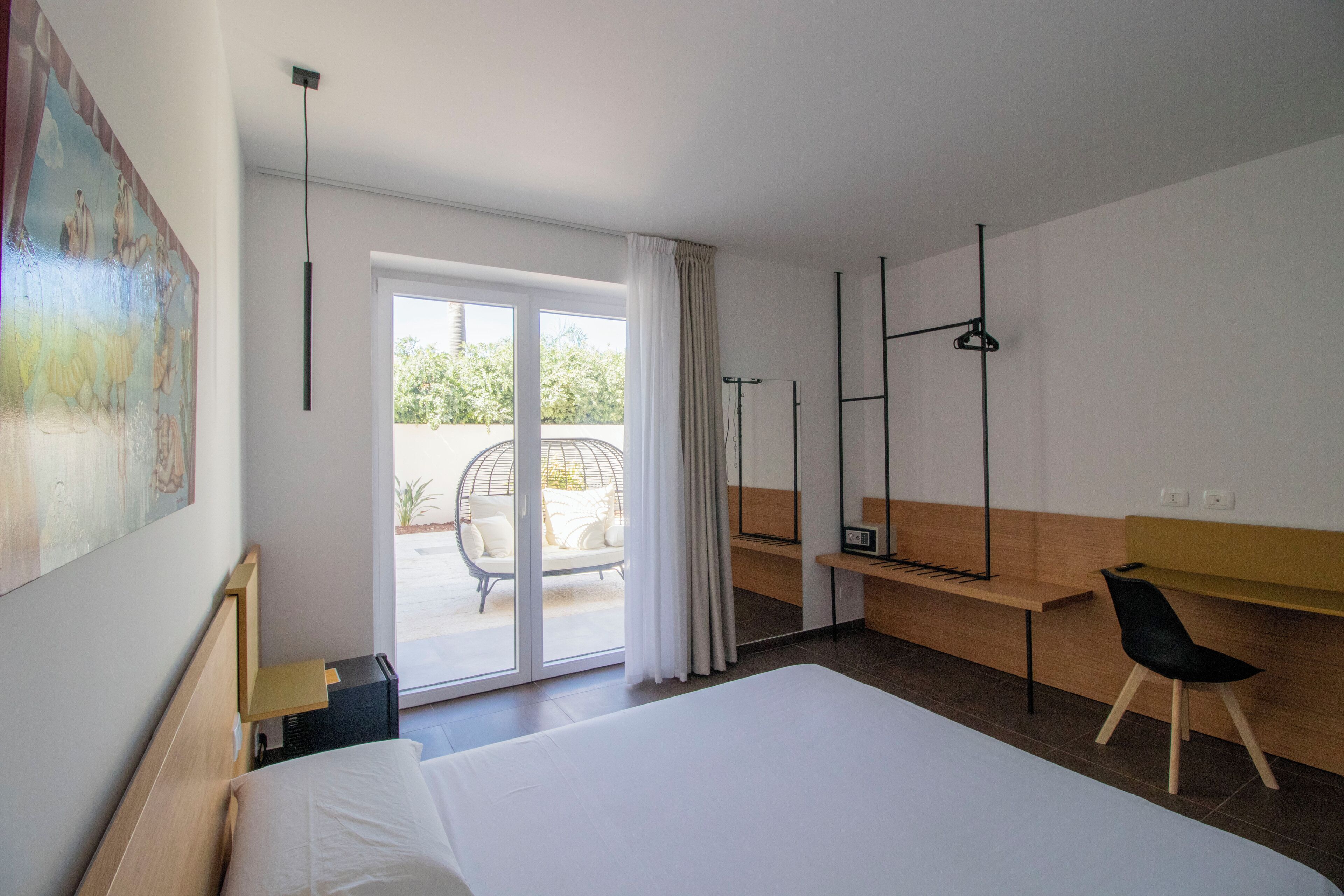 A modern hotel room with a large bed, a desk, a chair, and a view of the outdoors.