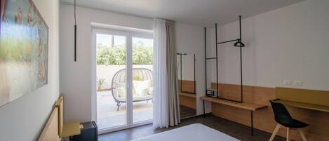 A modern hotel room with a large bed, a desk, a chair, and a view of the outdoors.