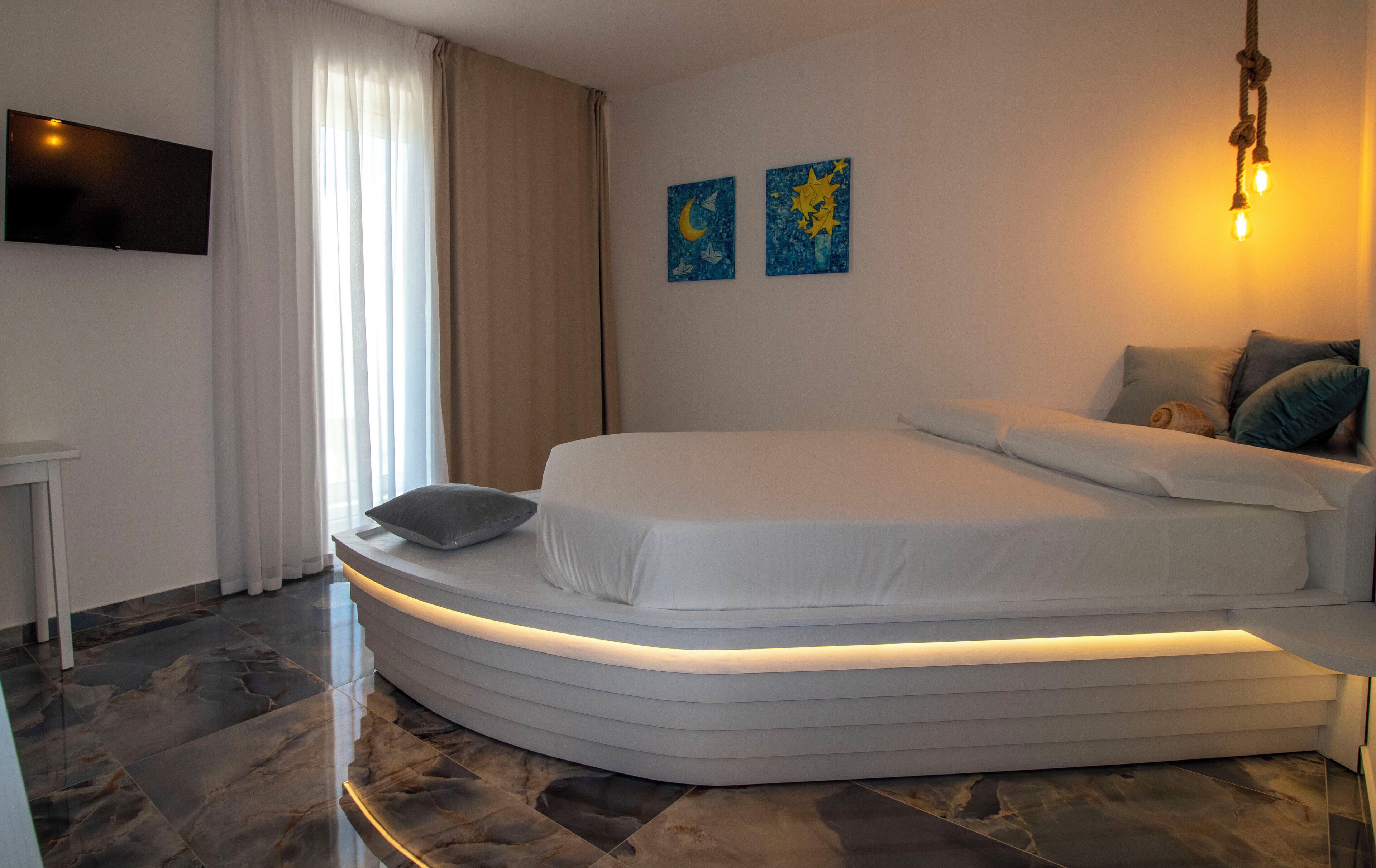 A modern bedroom with a curved bed, a flat-screen TV, and artwork on the wall.