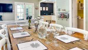 A dining area with a wooden table set for six, surrounded by white chairs. A ceiling fan is visible above the table, and a television is mounted on the wall to the left. - Alfie's Place - A period classic in central location (NULKABA)