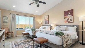 Une chambre d’hôtel avec deux lits, un bureau, une chaise, un ventilateur de plafond et une grande fenêtre avec des rideaux.