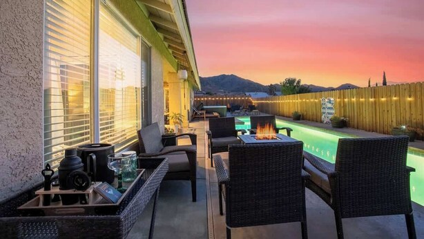 Une terrasse avec des sièges extérieurs, une piscine et une vue sur une chaîne de montagnes au coucher du soleil.