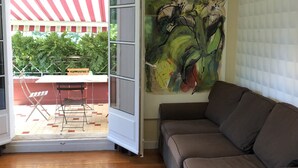 An open door leading to a patio with a striped awning, a brown sofa, and a large abstract painting on the wall. - G1 Apartment with beautiful terrace between Grenoble and Chamrousse (Saint-Martin-d'Uriage)