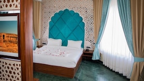 Habitación de hotel con una cama grande, un cabecero decorativo y vistas a un edificio a través de una ventana.