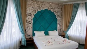 Una cama bien hecha con sábanas blancas y un cabecero verde azulado, rodeada de cortinas de colores claros y un panel decorativo en la pared.