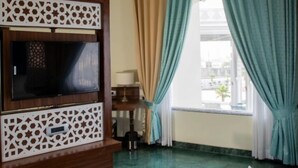 Habitación de hotel con televisor de pantalla plana, panel decorativo de madera, cama con pétalos de rosa, cortinas color turquesa y ventilador de techo.