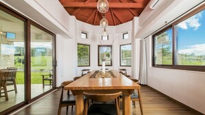 A dining area with a wooden table and chairs, large windows, and a view of the outdoors.