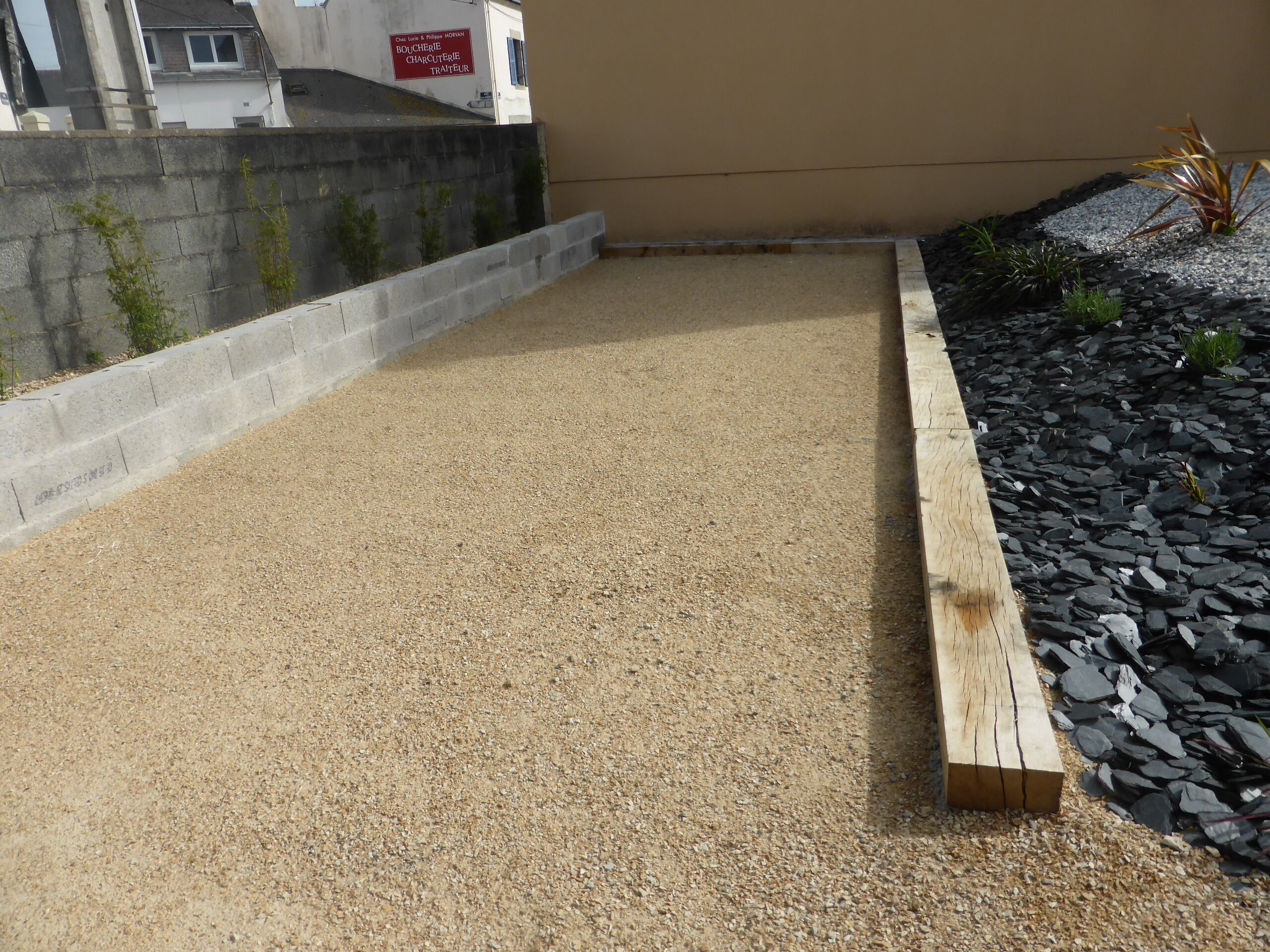 Eine Dachterrasse mit Kiesboden, einem Holzpflanzkasten mit schwarzen Steinen und einer kleinen Pflanze.