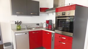 Une cuisine moderne avec des meubles de rangement rouges et gris, un lave-vaisselle encastré et un four en acier inoxydable.