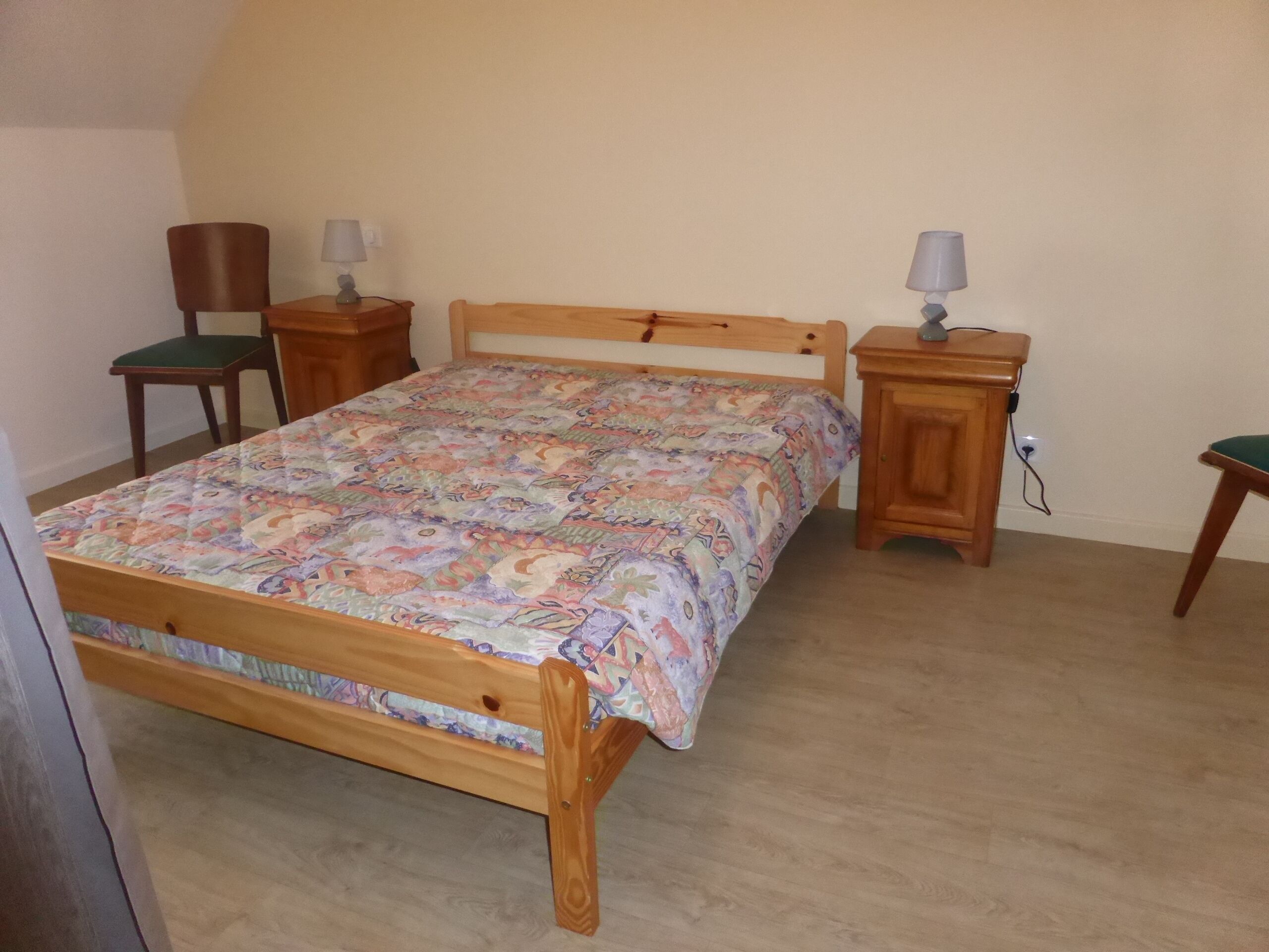 Un dormitorio con una cama de madera, dos mesitas de noche, una silla y una lámpara.