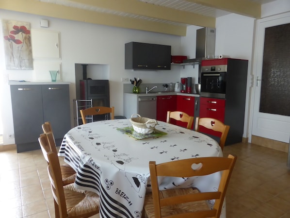 A dining area with a round table, chairs, and a kitchen in the background.