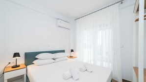 Ein Hotelzimmer mit einem Bett, zwei Nachttischen mit Lampen, einem Fenster mit transparenten Vorhängen und einer Klimaanlage an der Wand.
