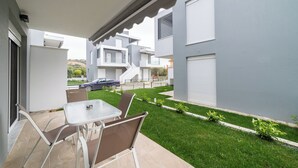 Eine moderne Terrassenausstattung mit Tisch und Stühlen, ein geparktes Auto im Hintergrund und einem gepflegten Rasen.