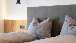 Un letto con una testiera grigia, un pannello di legno a parete e una lampada a sospensione nera.