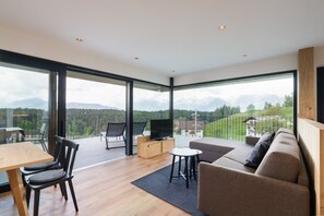Un salon moderne doté d’un grand mur de verre, d’un canapé, d’un téléviseur posé sur un meuble en bois et d’un coin repas avec des chaises et une table.