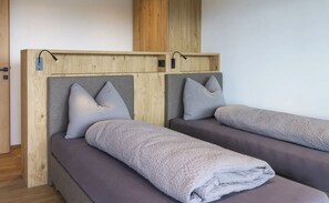Zwei Einzelbetten mit grauen Kopfteilen und Kissen, Holzvertäfelung an den Wänden und eine Holztür.
