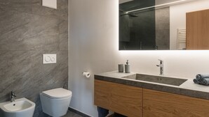 Moderni kylpyhuone, jossa on bidee, wc, peilillä varustettu pesuallas ja pyyhekoukku.