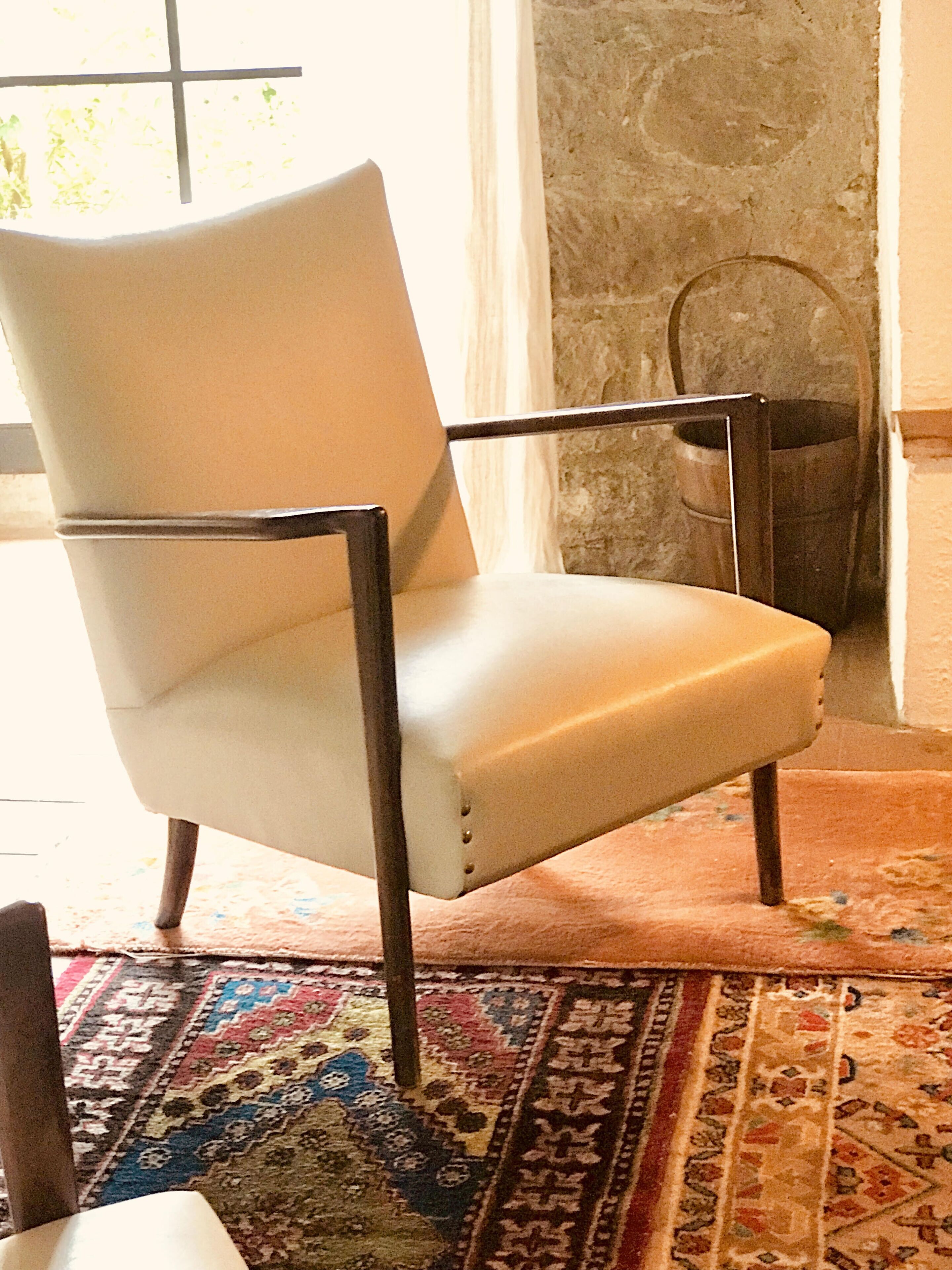 Un fauteuil blanc aux pieds en métal, dans une pièce dotée d’un tapis à motifs et d’un mur en pierre.