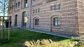 Ein mehrstöckiges Backsteingebäude mit rotem Dach, großen Fenstern und einem gepflegten Rasen mit Gras und Pflanzen.