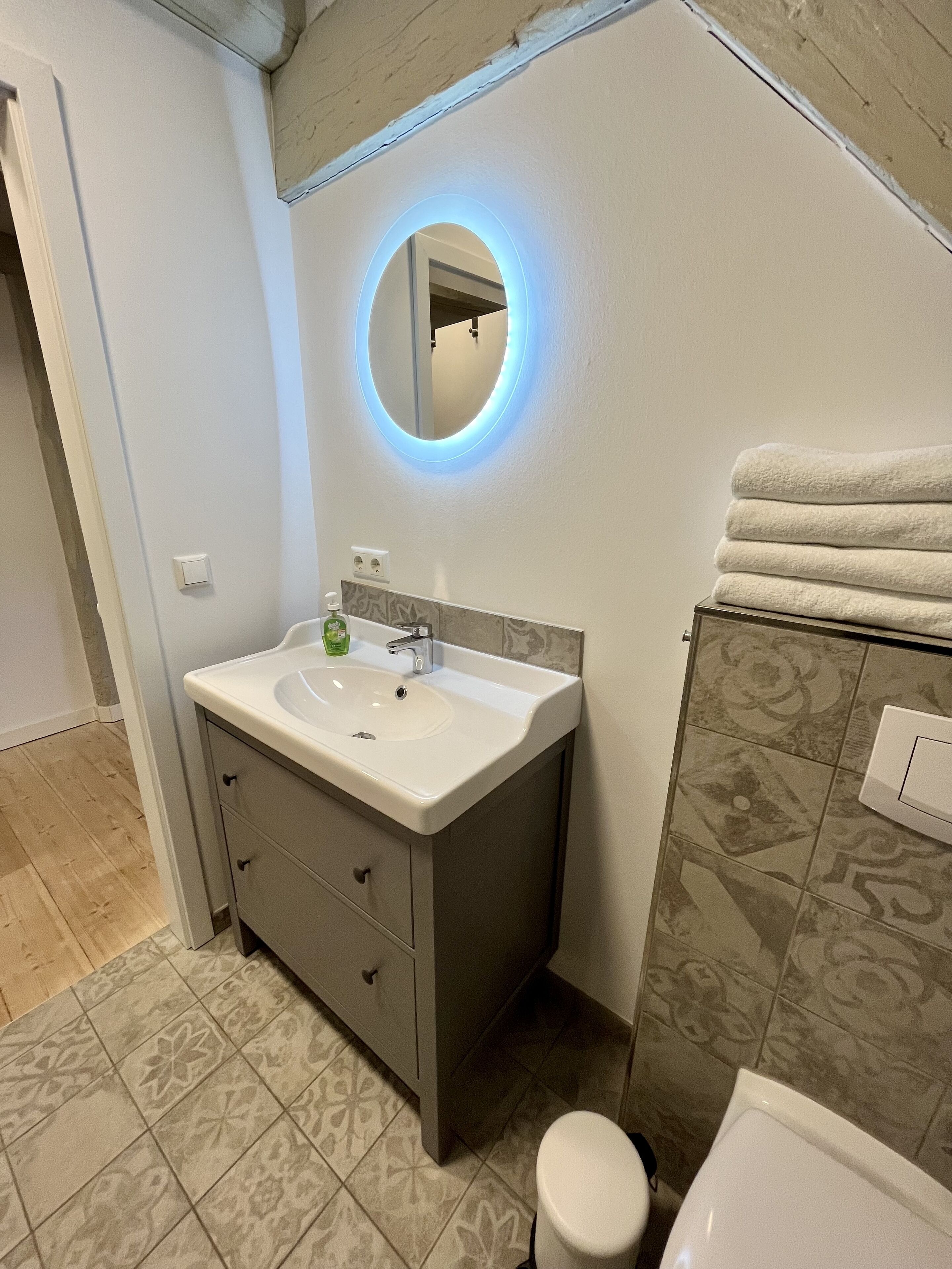 A bathroom with a white sink, a mirror with a blue light, and patterned tiles.