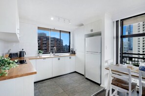 A modern kitchen with white cabinets, a stainless steel refrigerator, and a window with a view of high-rise buildings.