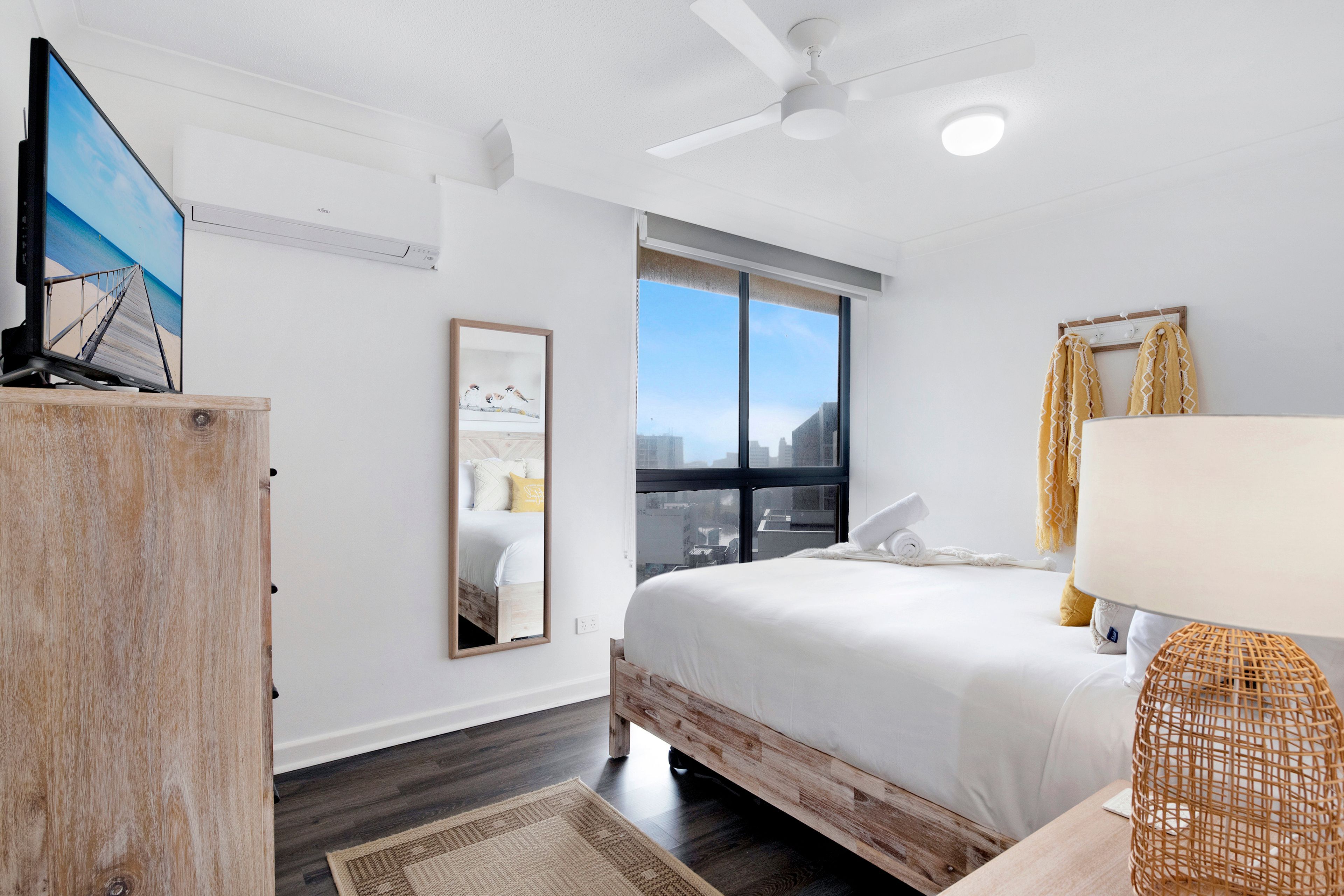 A modern bedroom with a bed, a TV, a window, and a ceiling fan.