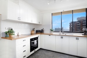 A modern kitchen with white cabinets, a wooden countertop, a built-in oven, and a window with a city view.