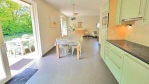 A modern kitchen with light green cabinets, a dining area with a table and chairs, and a view of greenery outside. - Modern holiday home with a large garden.  Near the beach (Callantsoog)