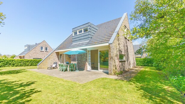 A modern house with a patio, a dining area, and a large window. - Modern holiday home with a large garden.  Near the beach (Callantsoog)