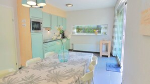 A modern kitchen with teal cabinets, a microwave, and a window overlooking greenery. - Modern holiday home with a large garden.  Near the beach (Callantsoog)