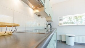 A modern kitchen with a stainless steel countertop, a coffee machine, and a window with a view of greenery. - Modern holiday home with a large garden.  Near the beach (Callantsoog)
