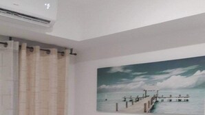 A hotel room with a bed, an air conditioning unit, a nightstand, and a painting of a pier. - Azure Condotel  (Parañaque)