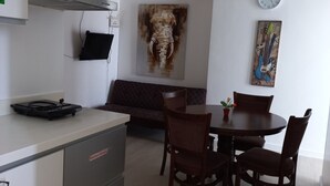 A modern kitchen with a dining area. It includes a stove, a sink, and a dining table with chairs. There is a clock on the wall and a painting above the dining table. - Azure Condotel  (Parañaque)