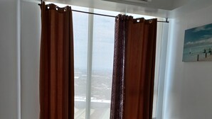 A room with a large window, brown curtains, a white ceiling, and a painting on the wall. - Azure Condotel  (Parañaque)