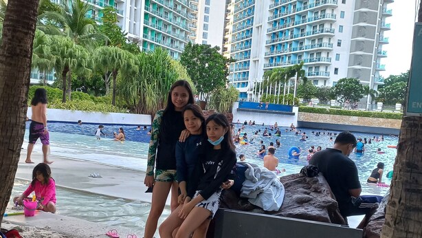A beach area with a sign reading "the azure beach," palm trees, and a pool with people swimming. - Azure Condotel  (Parañaque)