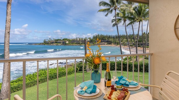 A balcony with a view of the ocean, a table set with a bottle of champagne, a plate of cheese, and a vase of flowers. - Napili Shores A202 Of Studio 1 Bedroom Condo by RedAwning (Lahaina)