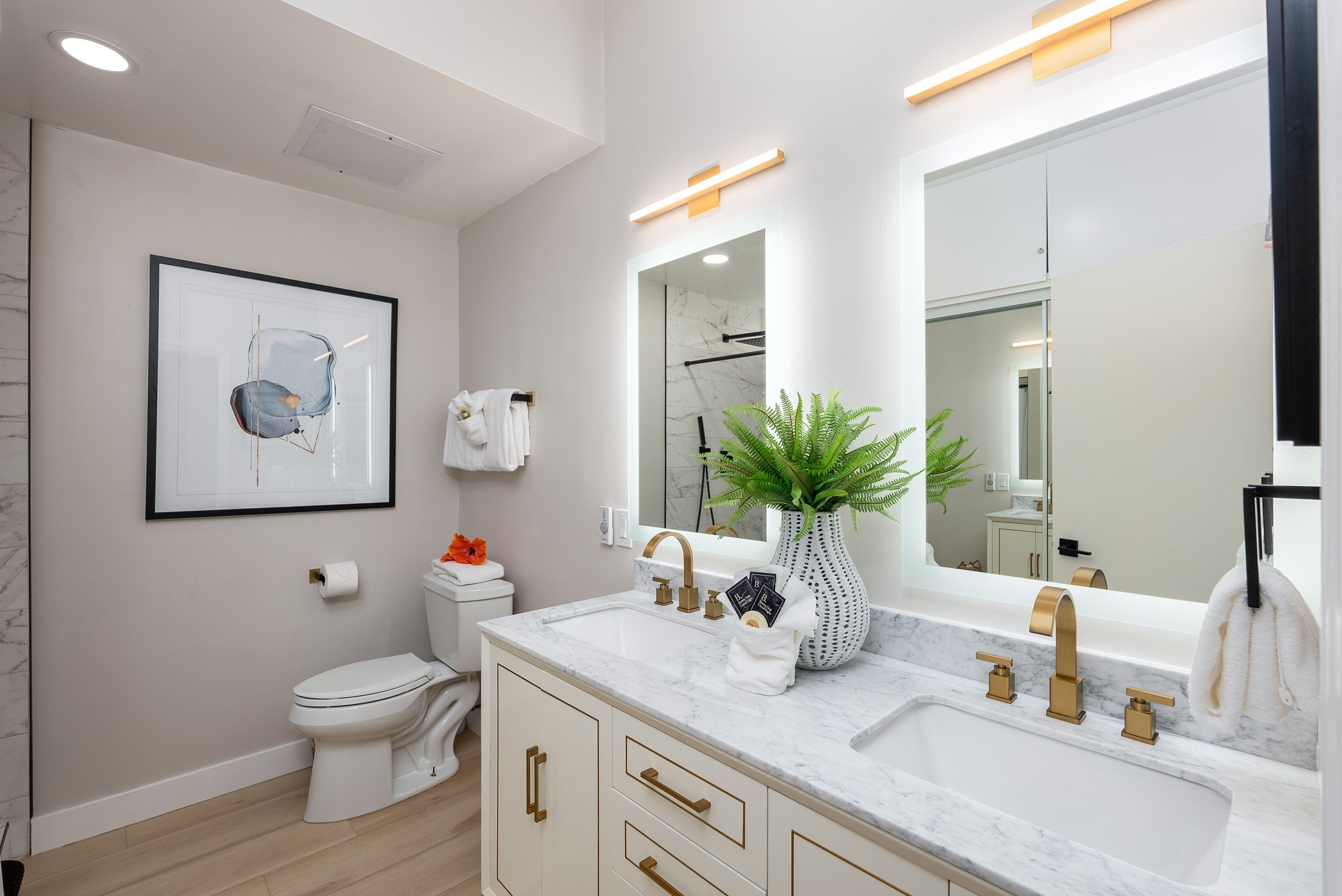 Une salle de bain moderne avec des toilettes blanches, un lavabo doté de robinetterie dorée et un grand miroir.