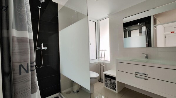A modern bathroom with a glass shower enclosure, a toilet, and a vanity with a glass countertop.